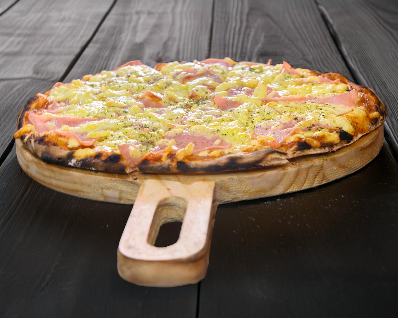 Freshly baked ham and pineapple pizza on a wooden board, perfect for sharing.