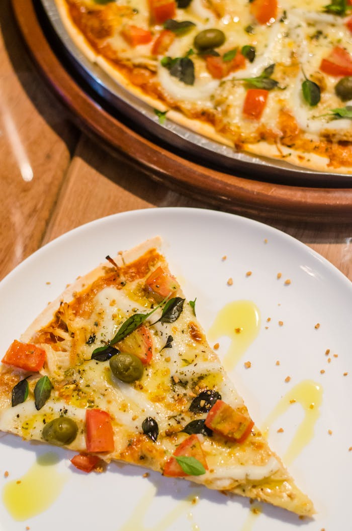 Close-up of a delicious pizza slice with toppings like cheese, olives, and tomatoes on a white plate.